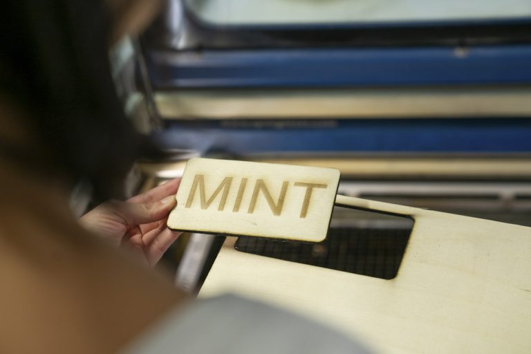 Unternehmerinnen halten ein Stück Holz mit der Aufschrift „Mint“ in der Hand.