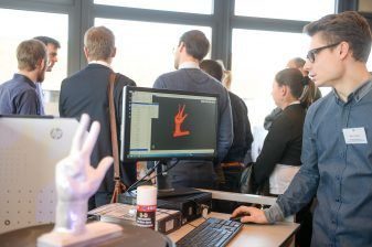 Ein 3D-gedrucktes Modell einer Hand, das man auch auf einem Bildschirm sieht.