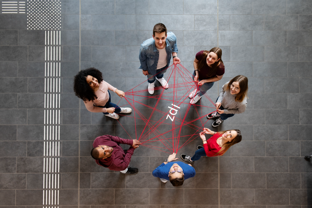 A group of people hold a network made of a red thread with the letters zdi on it.