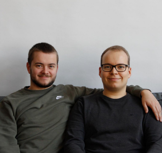 The photo shows Stefan and Philipp Lindner. They sit next to each other in front of a white wall and smile at the camera. Stefan put his arm around Philipp.
