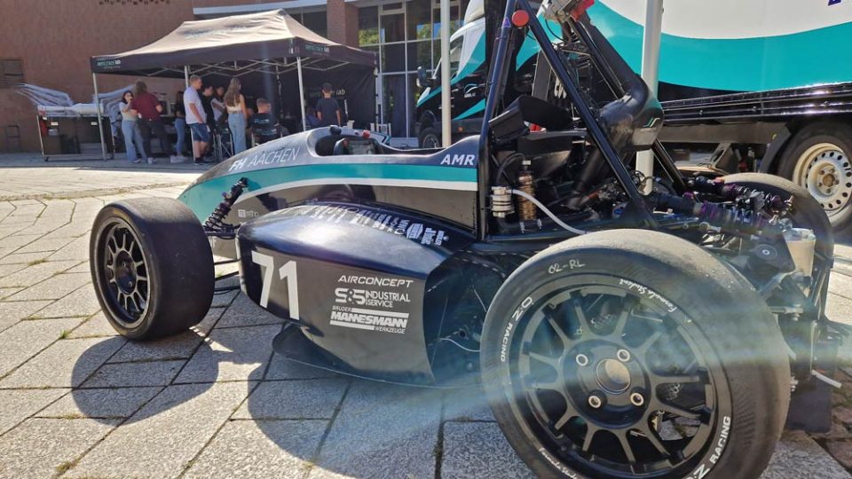 На фотографії зображений гоночний автомобіль на стенді AERO Race Lab в Ахенському університеті прикладних наук. Ви можете побачити їхній стенд на задньому плані.