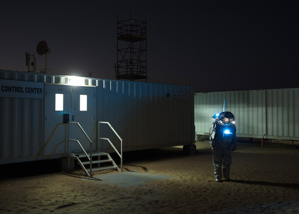 Кармен Келер стоїть перед будівлею вночі, одягнена в скафандр.