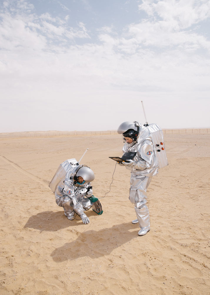 Two astronauts in spacesuits in the desert.