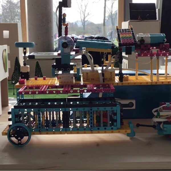 Eine mehrfarbige Robotermaschine, die auf einem Holztisch ausgestellt ist, im Hintergrund sind Modellhäuser zu sehen.