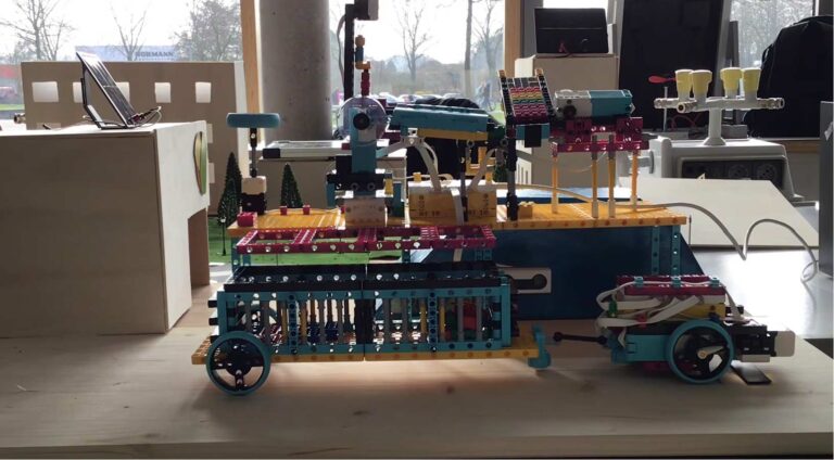 Разноцветная роботизированная машина на деревянном столе, на заднем плане видны модели домов.