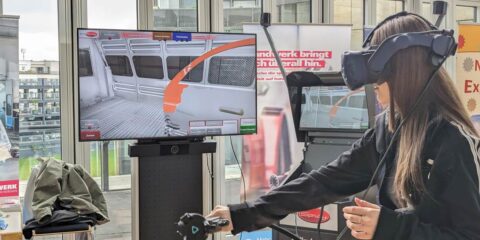 Auf der öffentlichen Ausstellung „Zukunftstag 2024“ setzt eine Frau ein VR-Headset auf. Sie interagiert mit einer Virtual-Reality-Simulation, die das Innere eines Zuges nachbildet.