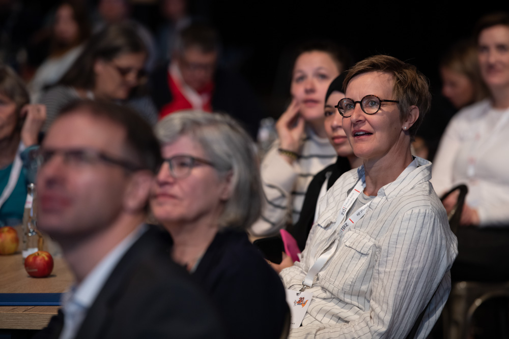 Mehrere Personen sitzen in einem Raum. Sie verfolgen aufmerksam eine Präsentation oder eine Person, die gerade spricht.