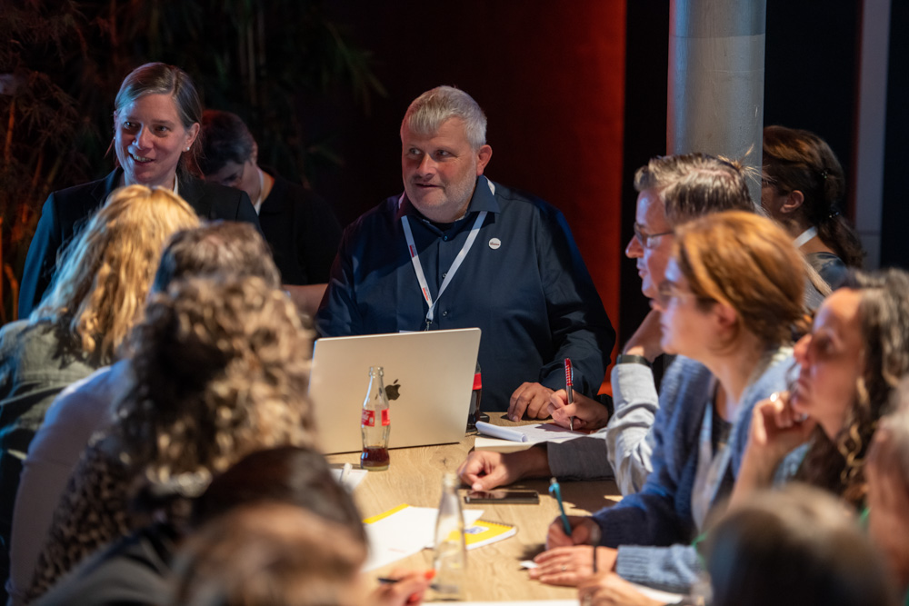 Mehrere Personen sitzen mit Notebooks und Laptops um einen Tisch herum. Sie diskutieren während einer Sitzung oder eines Workshops.