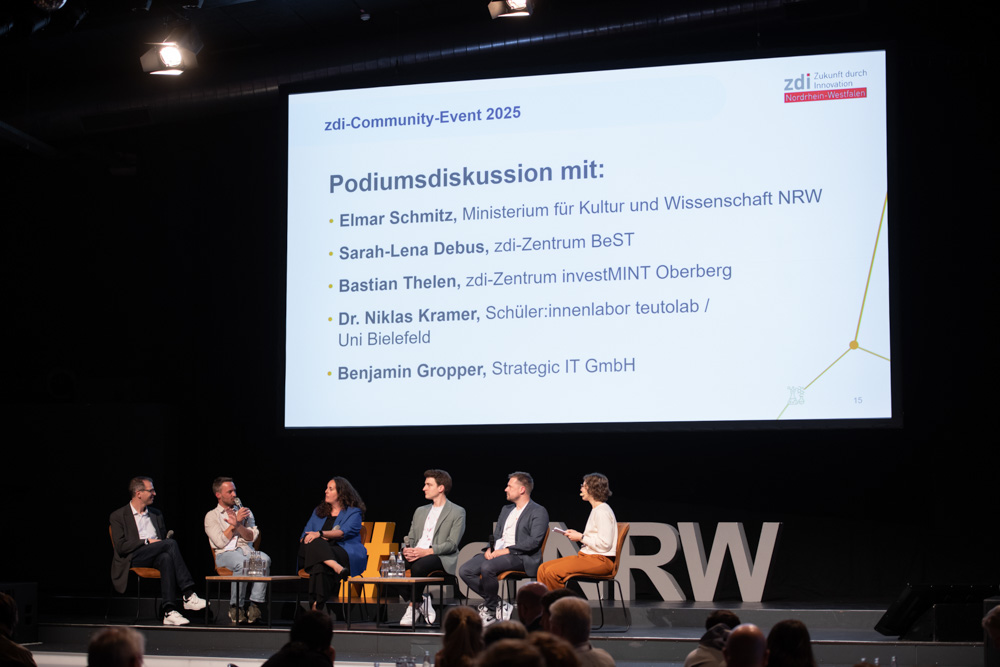 Fünf Podiumsteilnehmer sitzen auf der Bühne und diskutieren bei der zdi-Community-Veranstaltung 2025. Eine Leinwand hinter ihnen zeigt ihre Namen und Zugehörigkeiten.