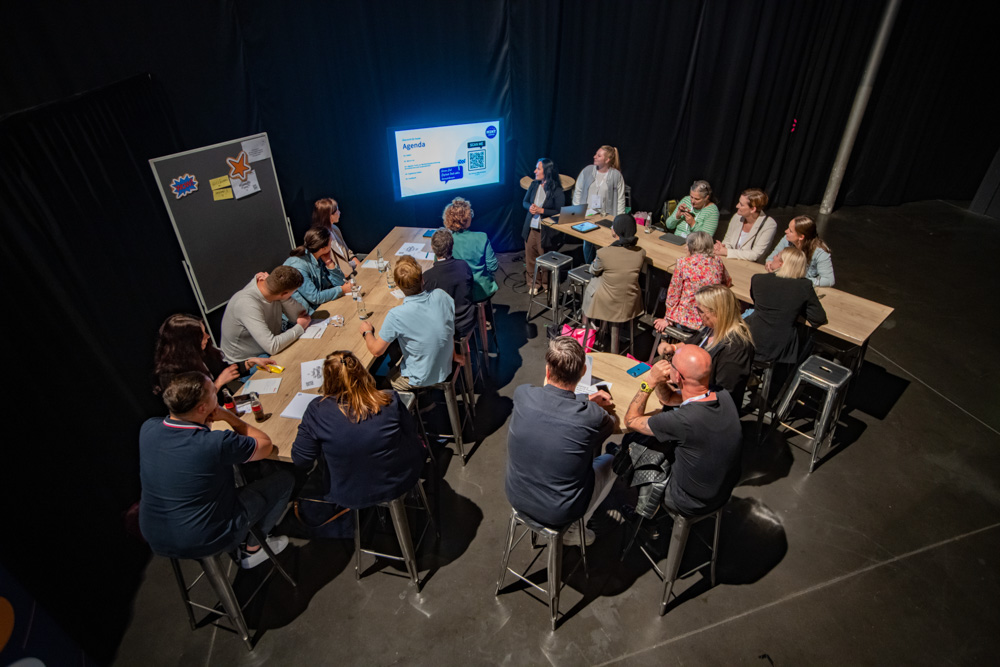 Das Foto zeigt eine Gruppe Menschen, die auf einen Bildschirm schauen. Zwei Frauen präsentieren hier digitale Tools.