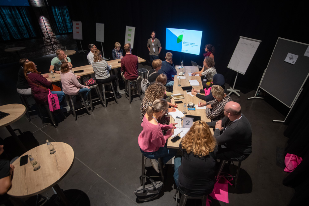 Das Foto zeigt eine Gruppe Menschen, die auf einen Bildschirm schauen. Ein Mann und eine Frau halten hier einen Vortrag.