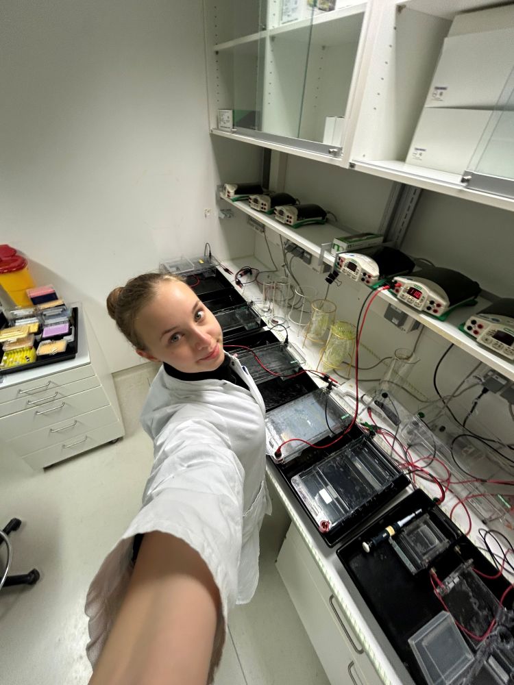 Das Foto zeigt Raja Flüchter, eine Frau mit langen Haaren im Laborkittel. Im Hintergrund sind technische Geräte zu sehen.