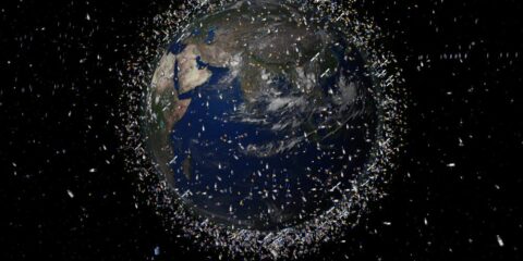 Die Abbildung zeigt die Erde, die von zahlreichen Weltraumtrümmern umgeben ist, wobei die Größe der Trümmer zur Verdeutlichung übertrieben dargestellt ist.