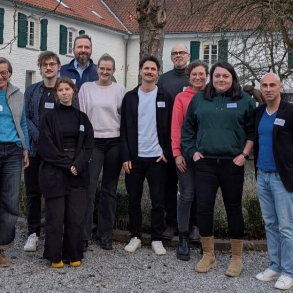 Zehn Personen stehen draußen und posieren für ein Foto vor einer runden Hecke und einem großen weißen Gebäude mit grünen Fensterläden.