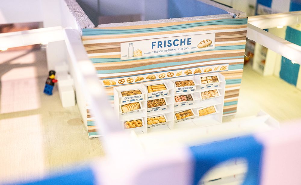 Das Bild zeigt eine kleine Bäckereiauslage in einem Miniaturgebäude mit Regalen voller Brot und Gebäck, über denen „Frische“ steht.