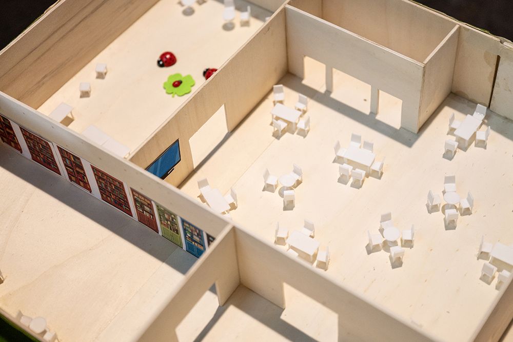 Das Bild zeigt das Innere eines Miniaturgebäudes mit kleinen Tischen, Stühlen, verspielten Dekorationen und Holzböden in offenen Räumen.