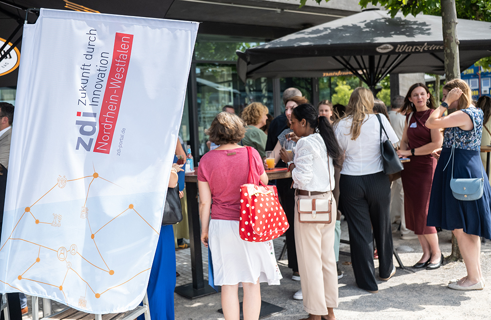 Menschen versammeln sich im Freien vor einem zdi-Banner und feiern die Verleihung des zdi-Qualitätssiegels 2026 in Nordrhein-Westfalen.